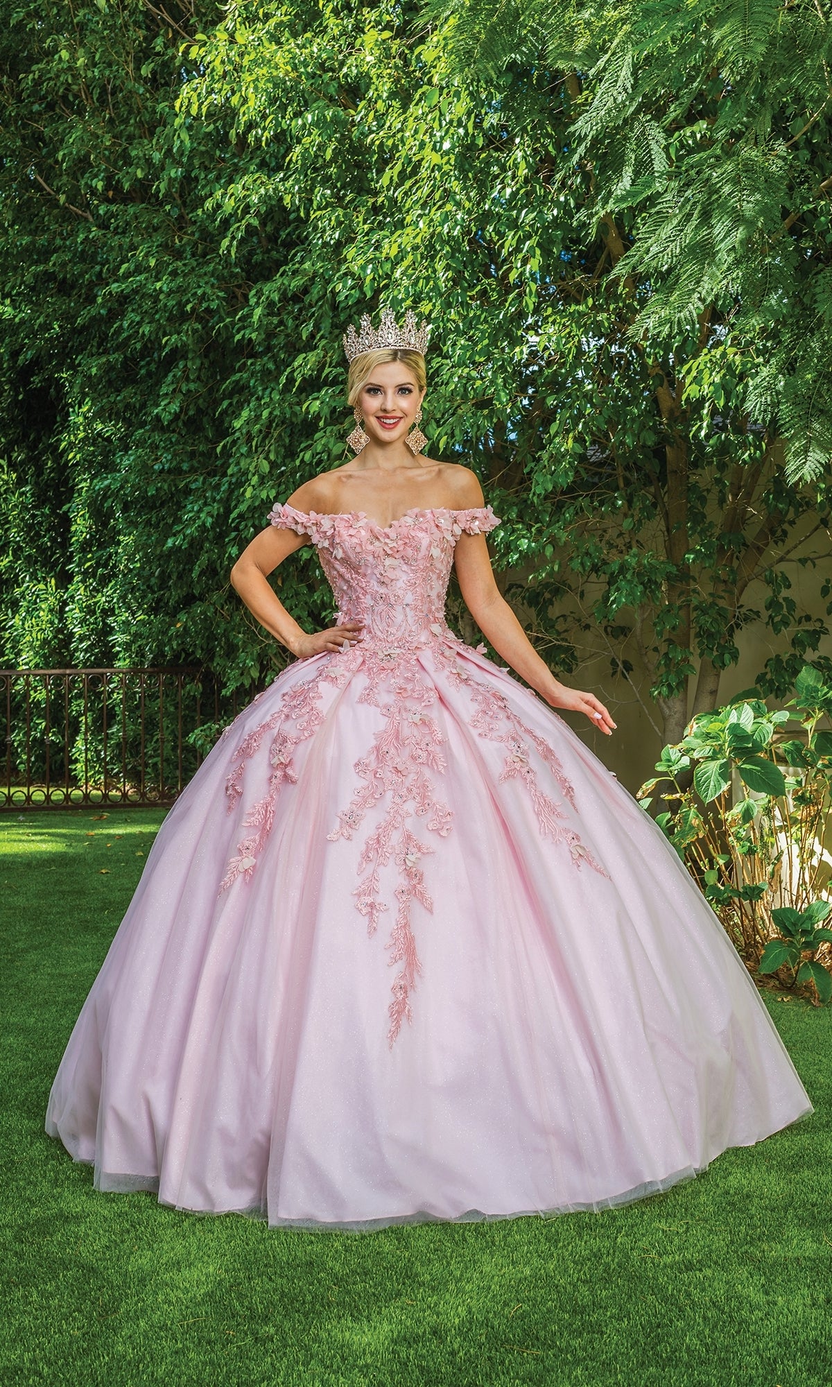 Someone wearing the Quinceanera Dress 1620 By Dancing Queen with floral embroidery and a tiara stands on grass in front of dense greenery.